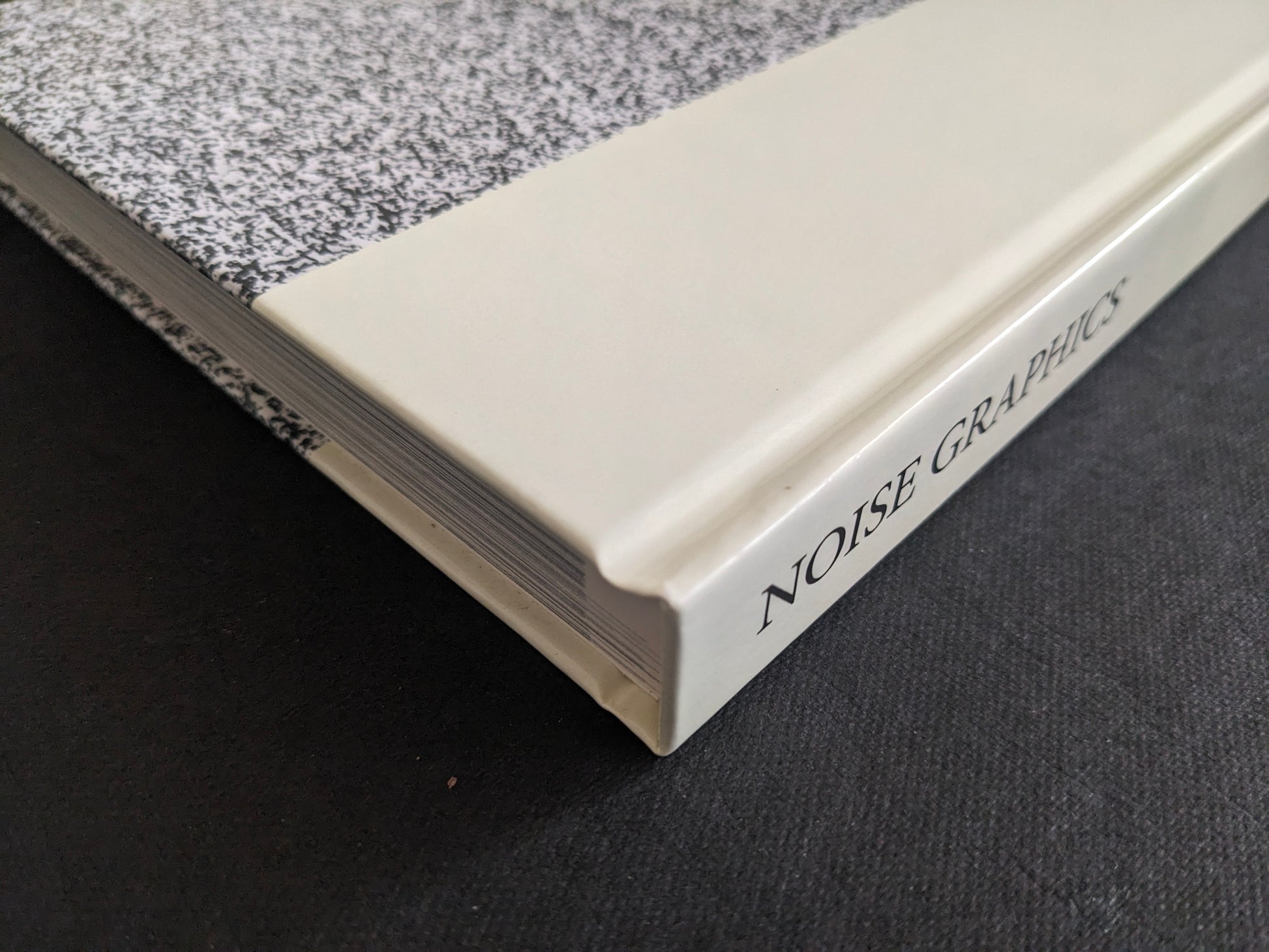 Noise Graphics 1980–1990 book spine detail with NOISE GRAPHICS title on a cream strip and a static-like black-and-white pattern.