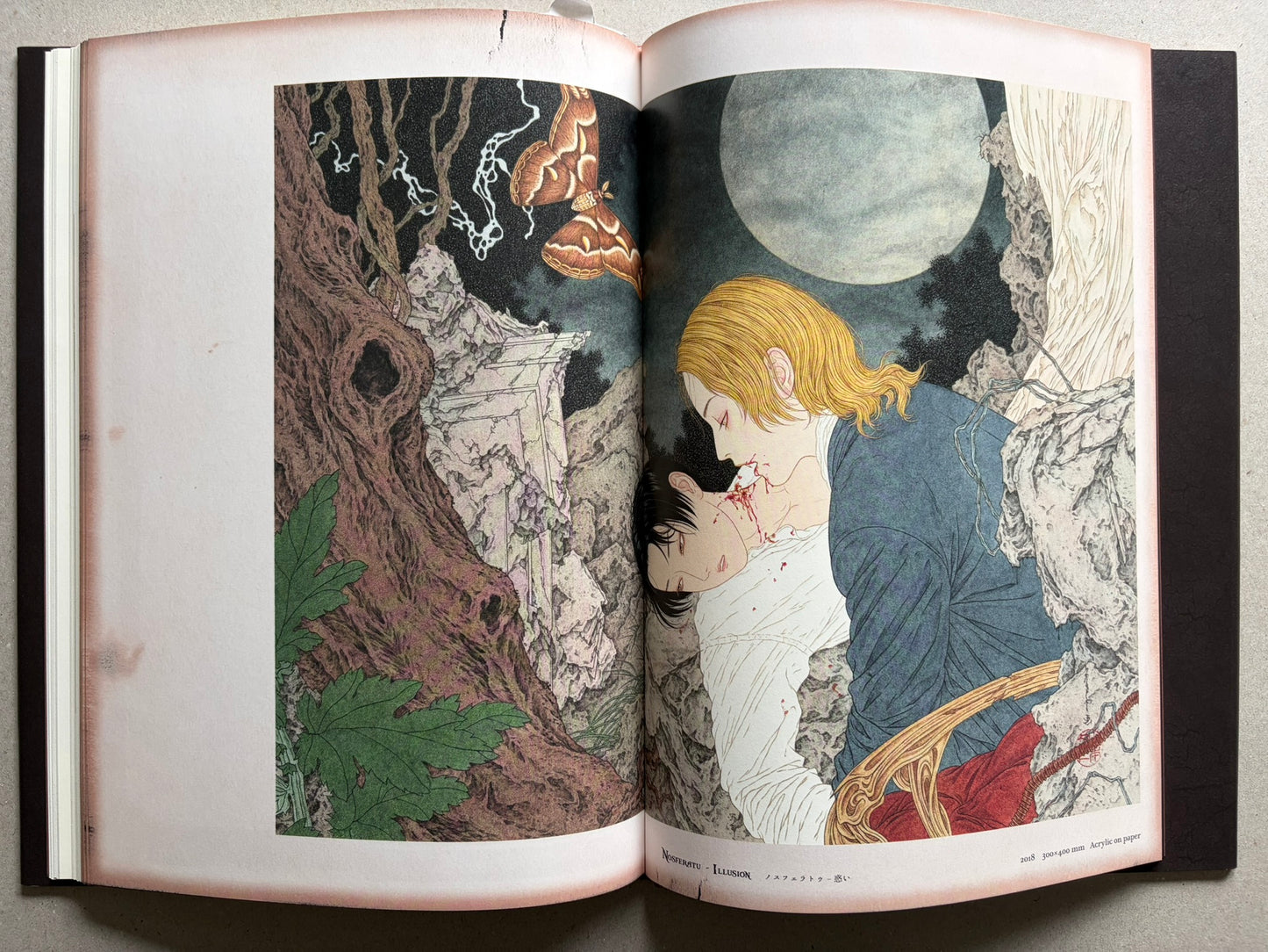 NOSFERATU by Takato Yamamoto, page spread with a blonde figure in blue clothing beside a pale face, under a large moon, with rocky trees and green leaves on the left page.