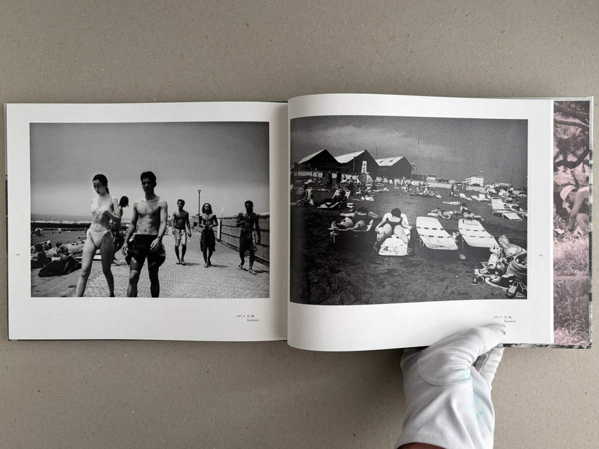 Open spread from Obi and Sand: Kyoto/Enoshima showing two black-and-white beach photographs, with a gloved hand holding the lower right corner of the book.