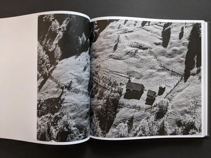 Aerial black and white photograph by Oleksandr Glyadyelov showing an isolated mountain village with wooden houses and fences in rural Ukraine.