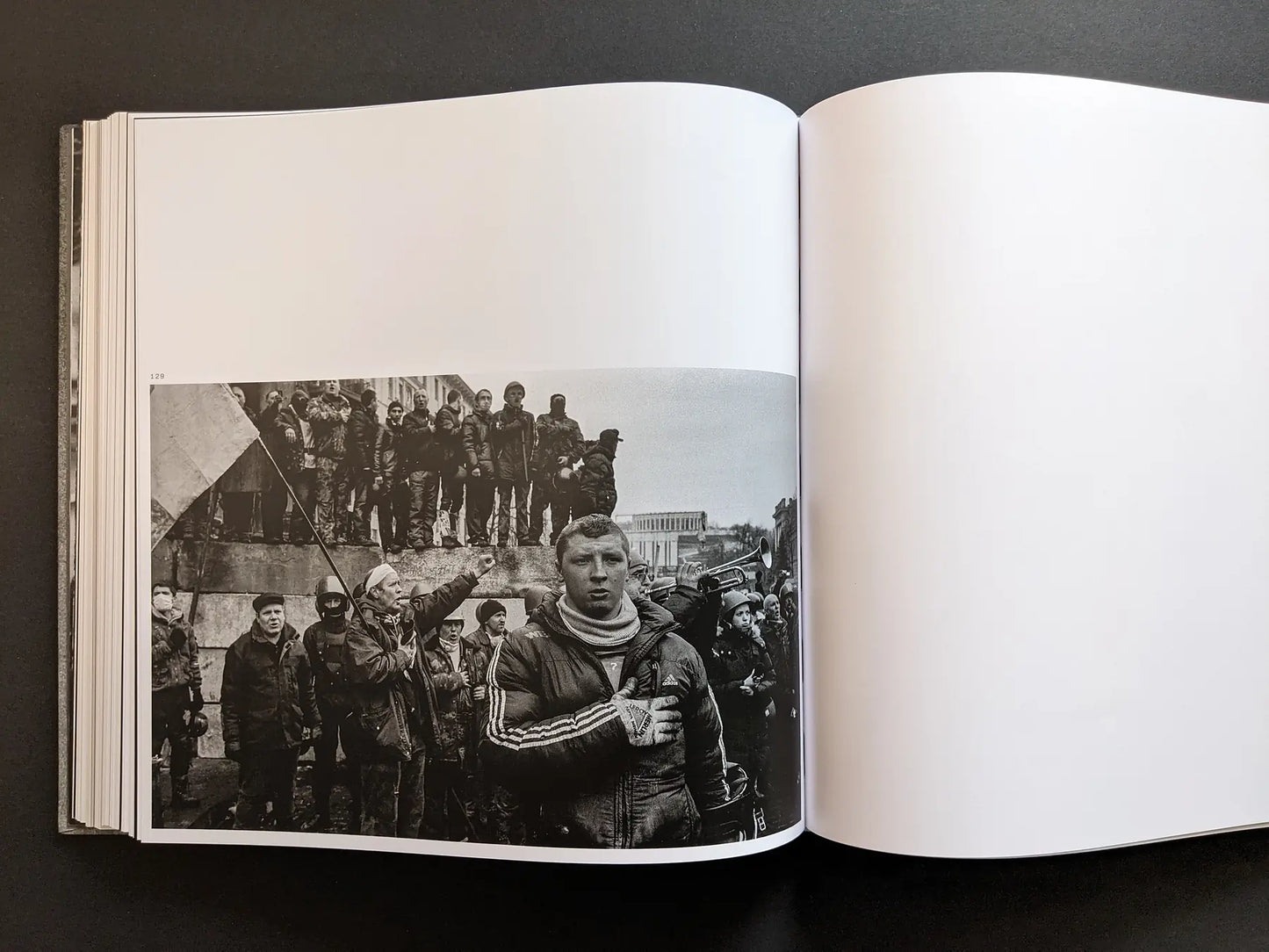 Black and white photograph by Oleksandr Glyadyelov of protesters gathered around a monument, one man holding a flag in the foreground.