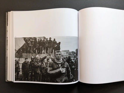 Black and white photograph by Oleksandr Glyadyelov of protesters gathered around a monument, one man holding a flag in the foreground.