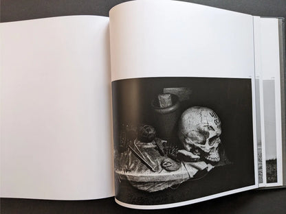 Still life photograph by Oleksandr Glyadyelov depicting a human skull, grenade and small objects arranged on a cloth in stark lighting.