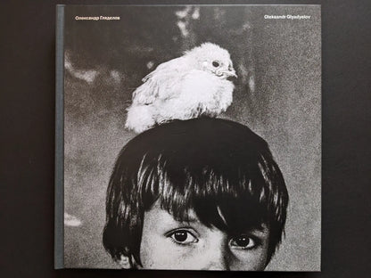 Front cover of Oleksandr Glyadyelov photobook showing a child’s face with a white bird perched on their head.