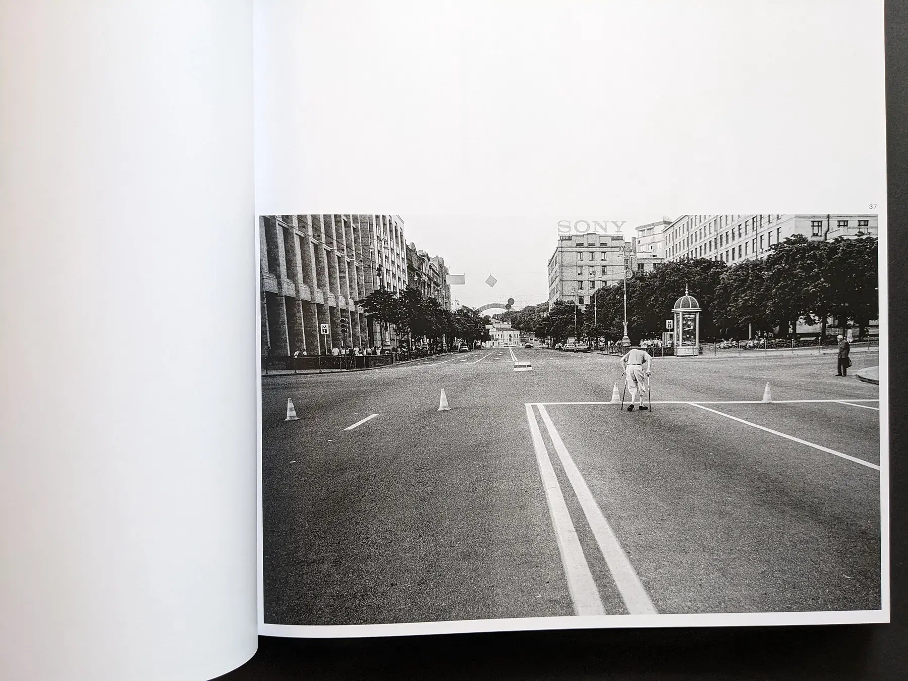 Inside spread from Oleksandr Glyadyelov showing a lone person with crutches crossing a wide, almost empty city avenue.