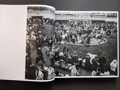 Inside spread from Oleksandr Glyadyelov depicting a crowded open-air market with stalls, vendors and shoppers seen from above.