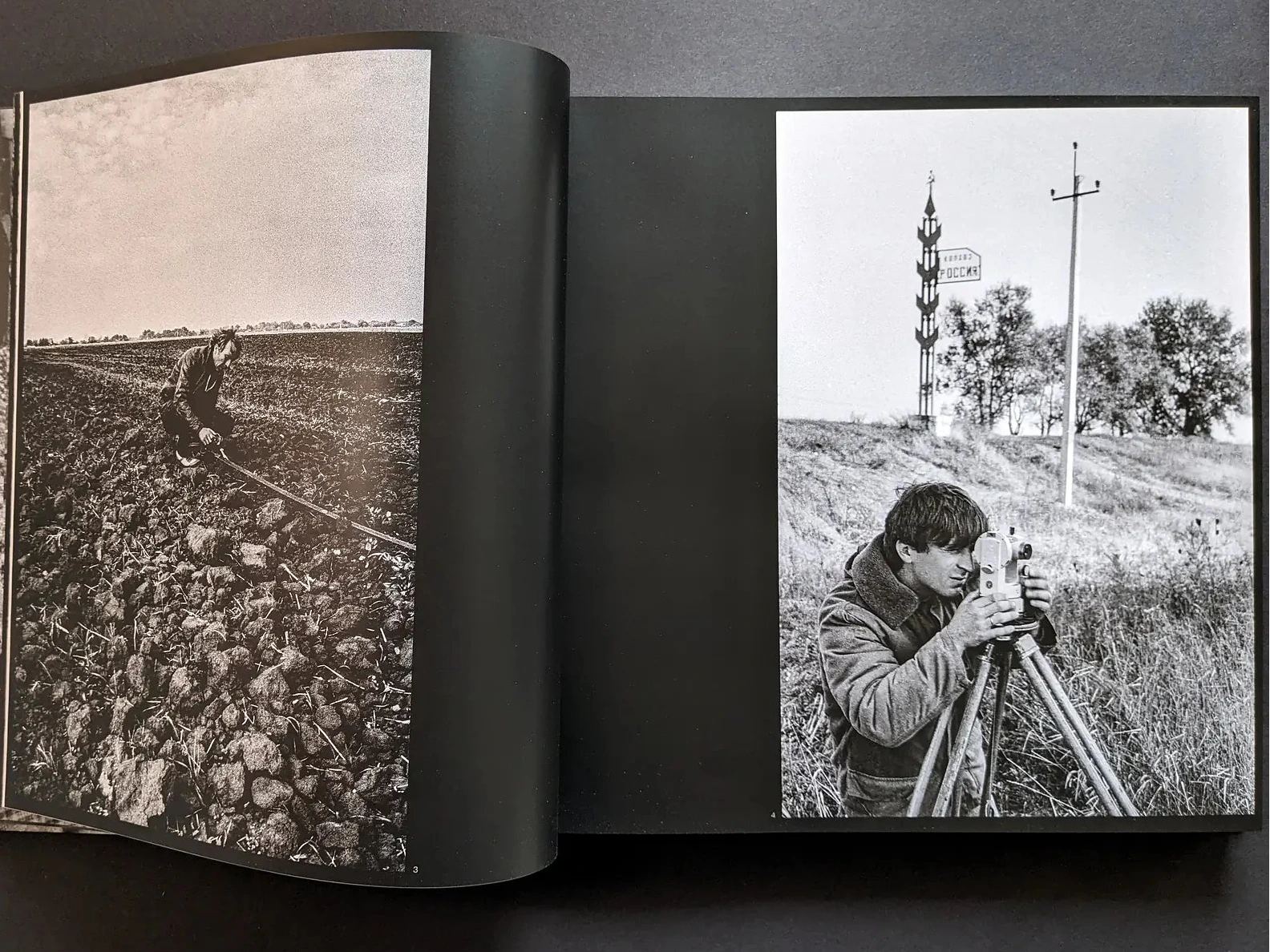 Inside spread from Oleksandr Glyadyelov showing a man working in a ploughed field and another using a surveyor’s tripod in open countryside.
