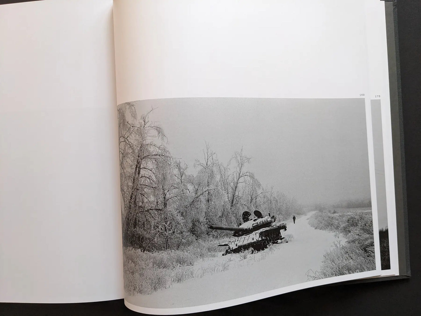 Double-page spread from “Oleksandr Glyadyelov” showing an abandoned tank in a snowy Ukrainian winter landscape with frost-covered trees.