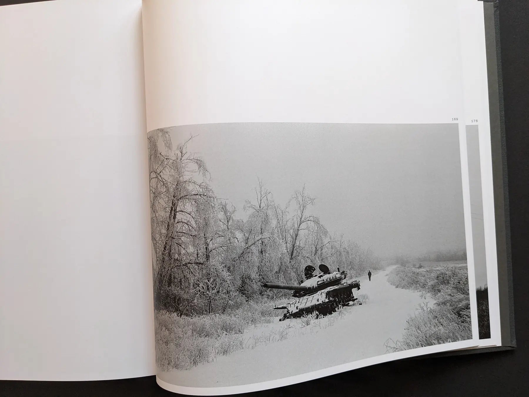 Double-page spread from “Oleksandr Glyadyelov” showing an abandoned tank in a snowy Ukrainian winter landscape with frost-covered trees.
