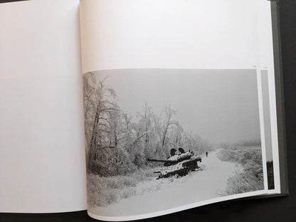 Double-page spread from “Oleksandr Glyadyelov” showing an abandoned tank in a snowy Ukrainian winter landscape with frost-covered trees.