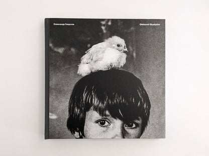 Front cover of Oleksandr Glyadyelov photobook showing a child’s face with a white bird perched on their head.