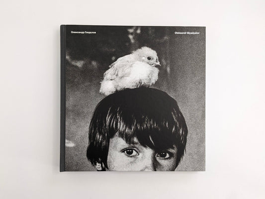 Front cover of Oleksandr Glyadyelov photobook showing a child’s face with a white bird perched on their head.