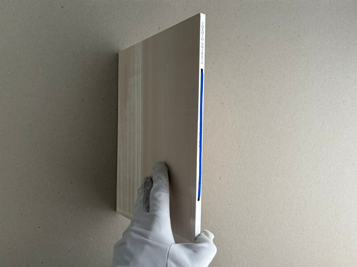 Painting – Toshio Shibata shown in side view, held upright by a gloved hand, with the blue ribbon on the spine visible.