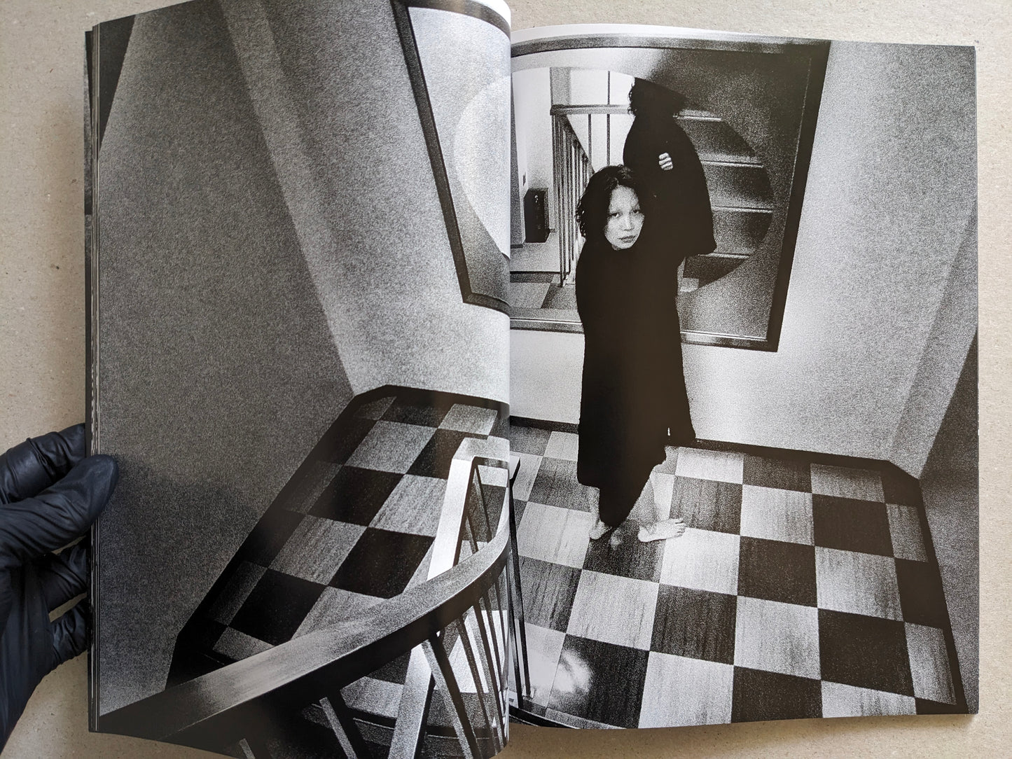 Woman in a dark coat standing in a stairwell with checkered floor, Record No. 50 by Daido Moriyama.