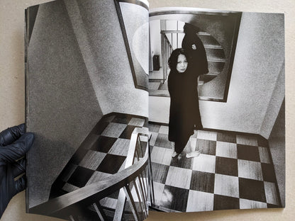 Woman in a dark coat standing in a stairwell with checkered floor, Record No. 50 by Daido Moriyama.