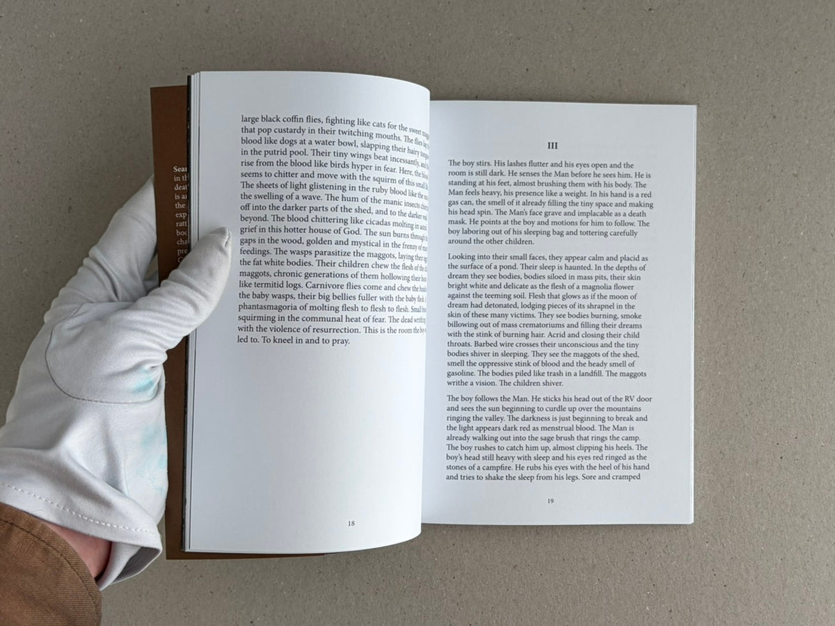 Open spread of Sacra by Sean M. Huber, showing pages 18 and 19 with dense black serif text and a gloved hand holding the book open.