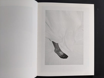 Monochrome close-up of a foot protruding from white bedsheets with darkened toes — Sleep Creek photobook.