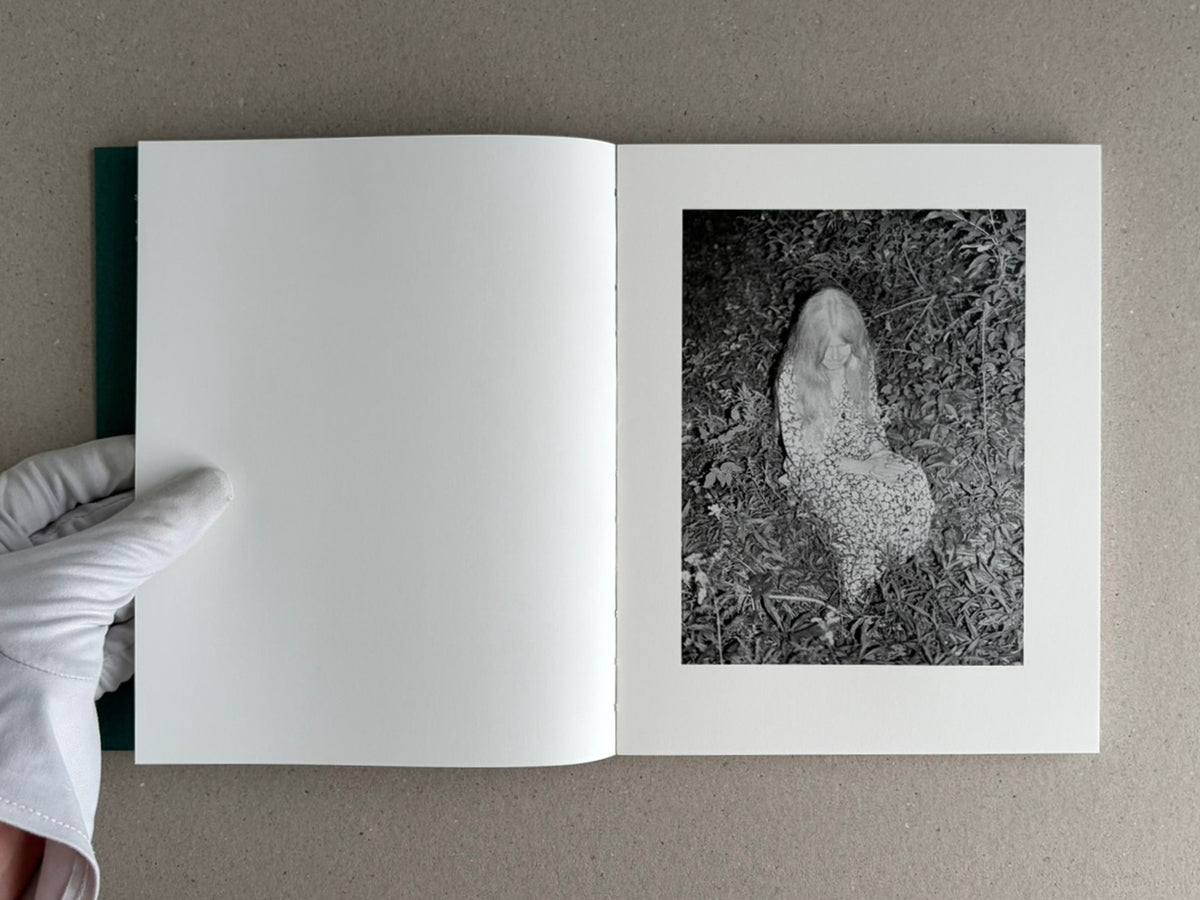 Open copy of Sleep Creek showing a blank left page and a black-and-white photograph of a seated figure in dense foliage on the right page.