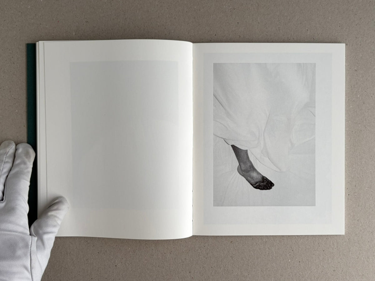 Open copy of Sleep Creek by Dylan Hausthor and Pia Paulina Guilmoth, showing a black-and-white spread with a cropped foot on the right page and a gloved hand holding the book at left.