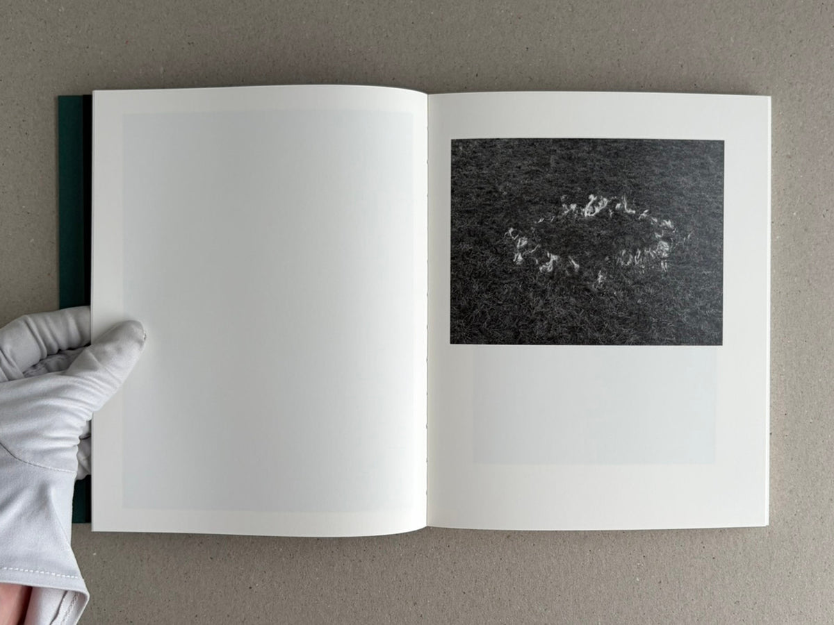 Open Sleep Creek photobook showing a blank left page and a black-and-white image on the right page, held open by a gloved hand.