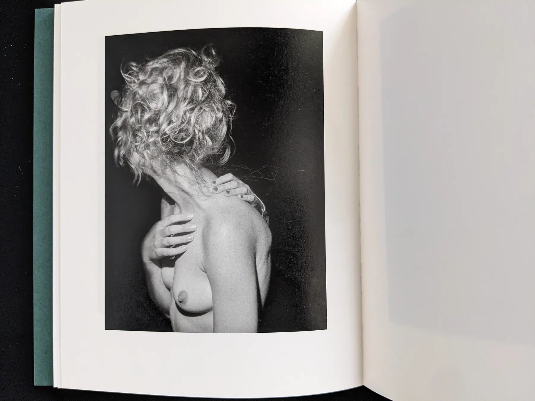 Black-and-white portrait of a nude figure with curly hair turned away, one arm across the chest.