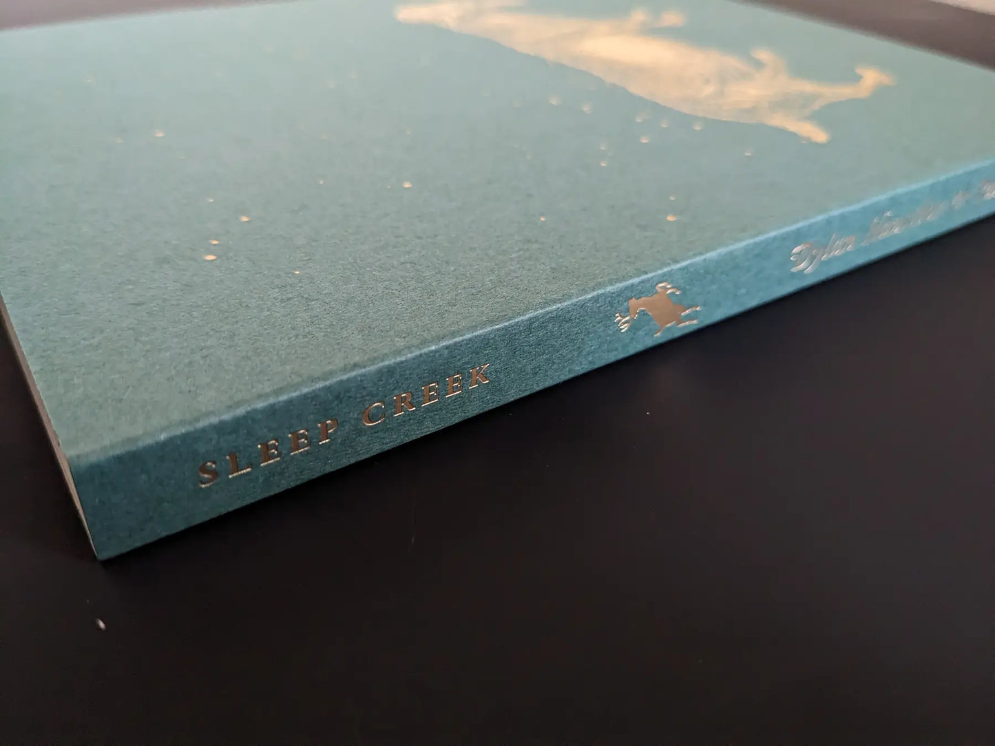 Book spine with gold-foil “SLEEP CREEK” title on green cover by Dylan Hausthor & Pia-Paulina Guilmoth.