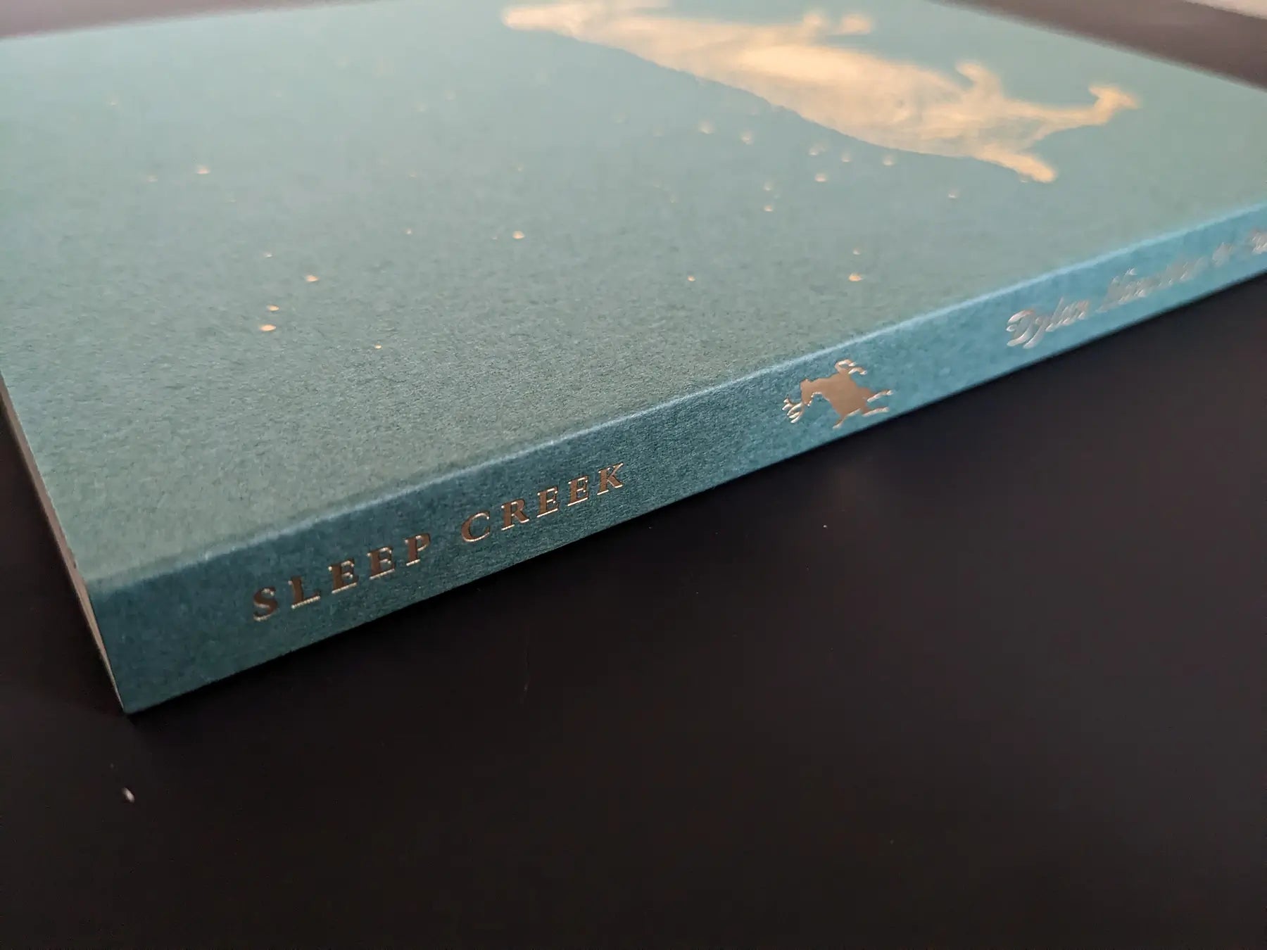 Book spine with gold-foil “SLEEP CREEK” title on green cover by Dylan Hausthor & Pia-Paulina Guilmoth.