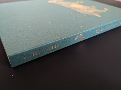 Book spine with gold-foil title “SLEEP CREEK” (Void open-spine softcover).