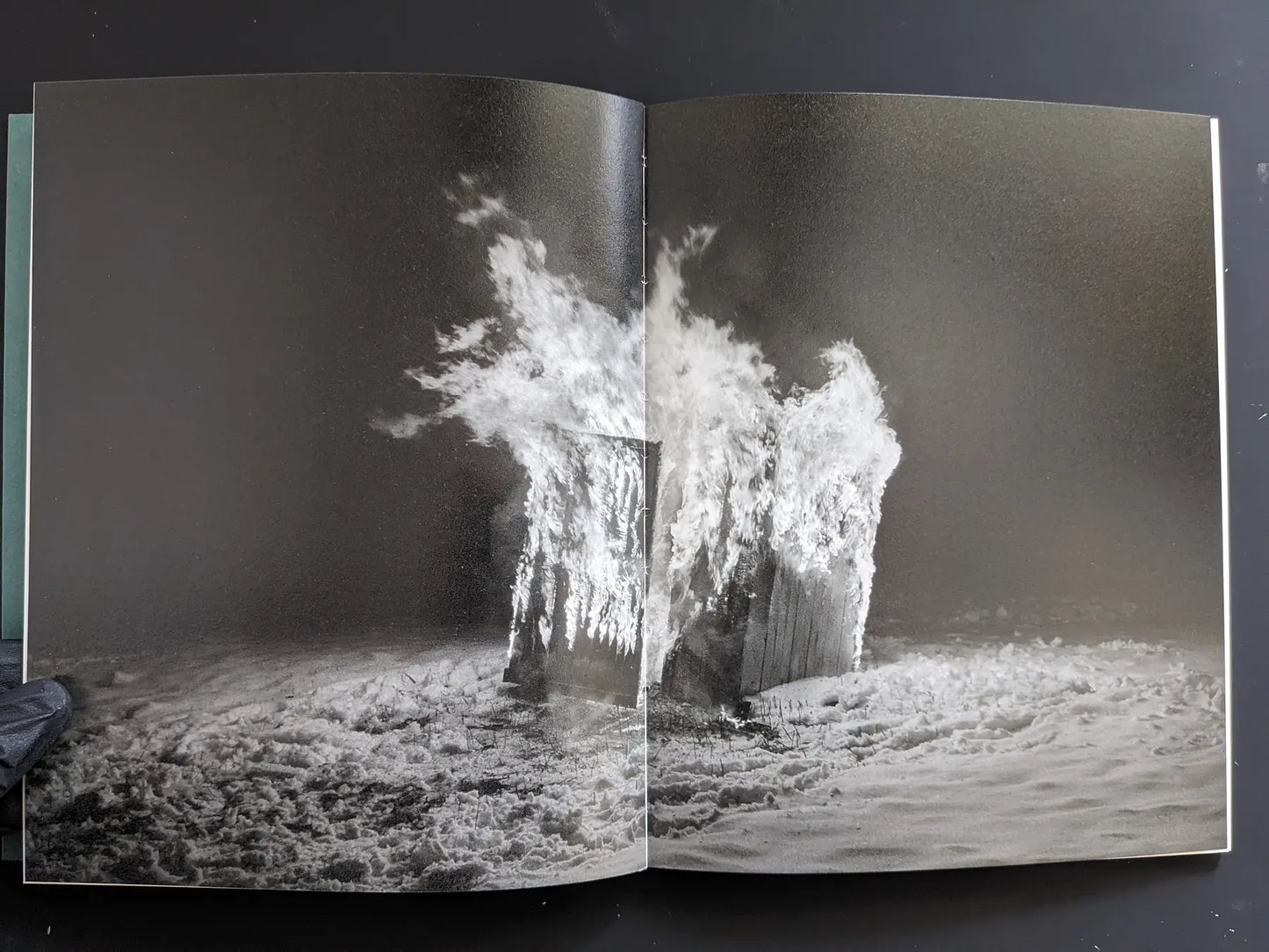 Double-page spread: small structure engulfed in flames at night within a snowy landscape.