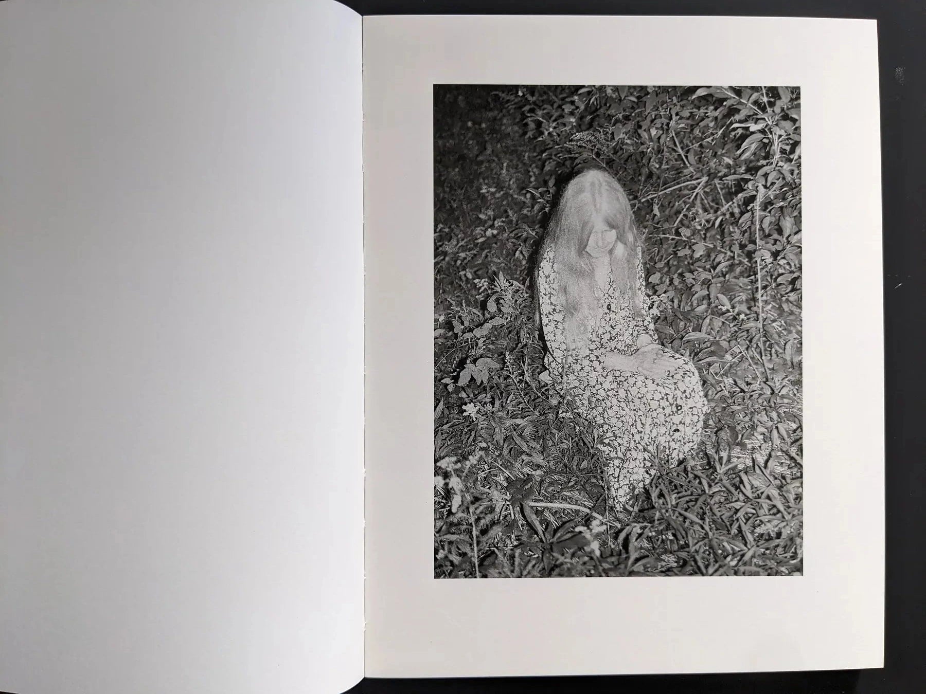 Black-and-white spread with a seated figure in dense foliage on the right page.