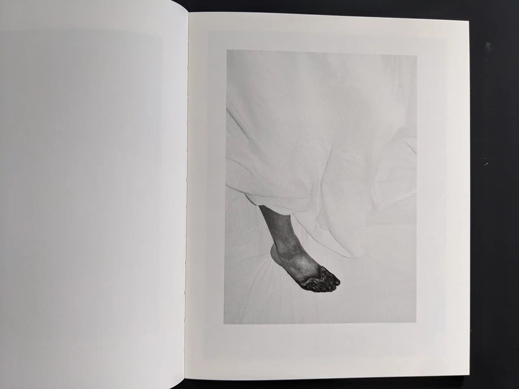 Close-up of a single foot emerging from white bedsheets.