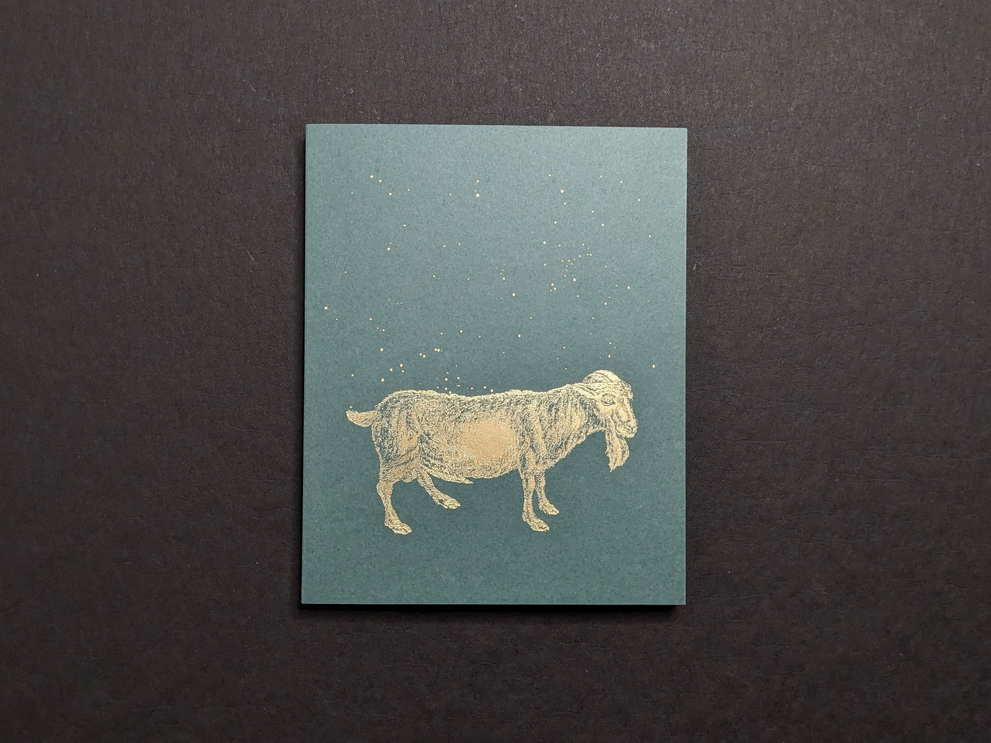 Front cover: teal board with a gold-foil goat and scattered dots.