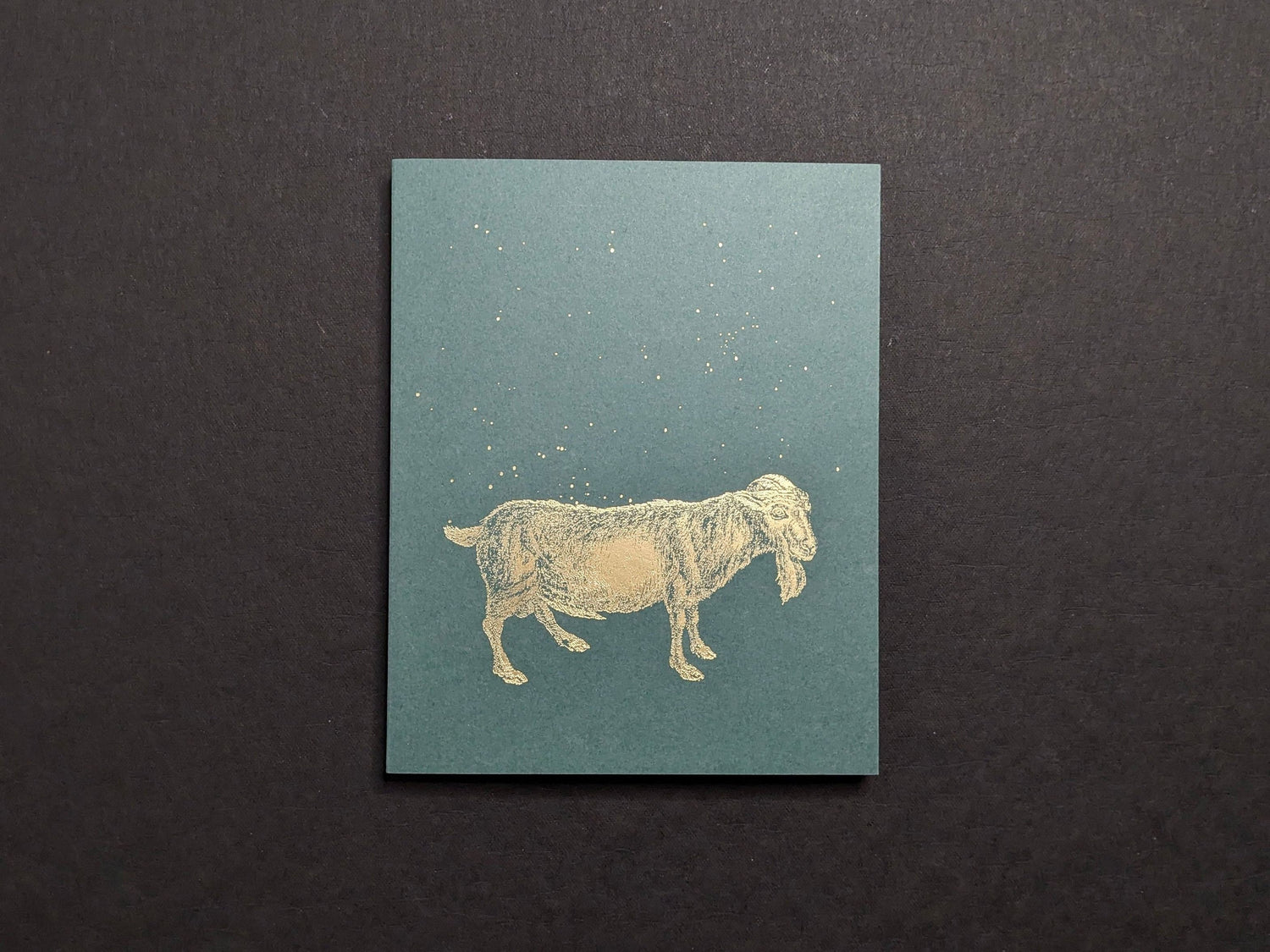 Front cover: teal board with a gold-foil goat and scattered dots.