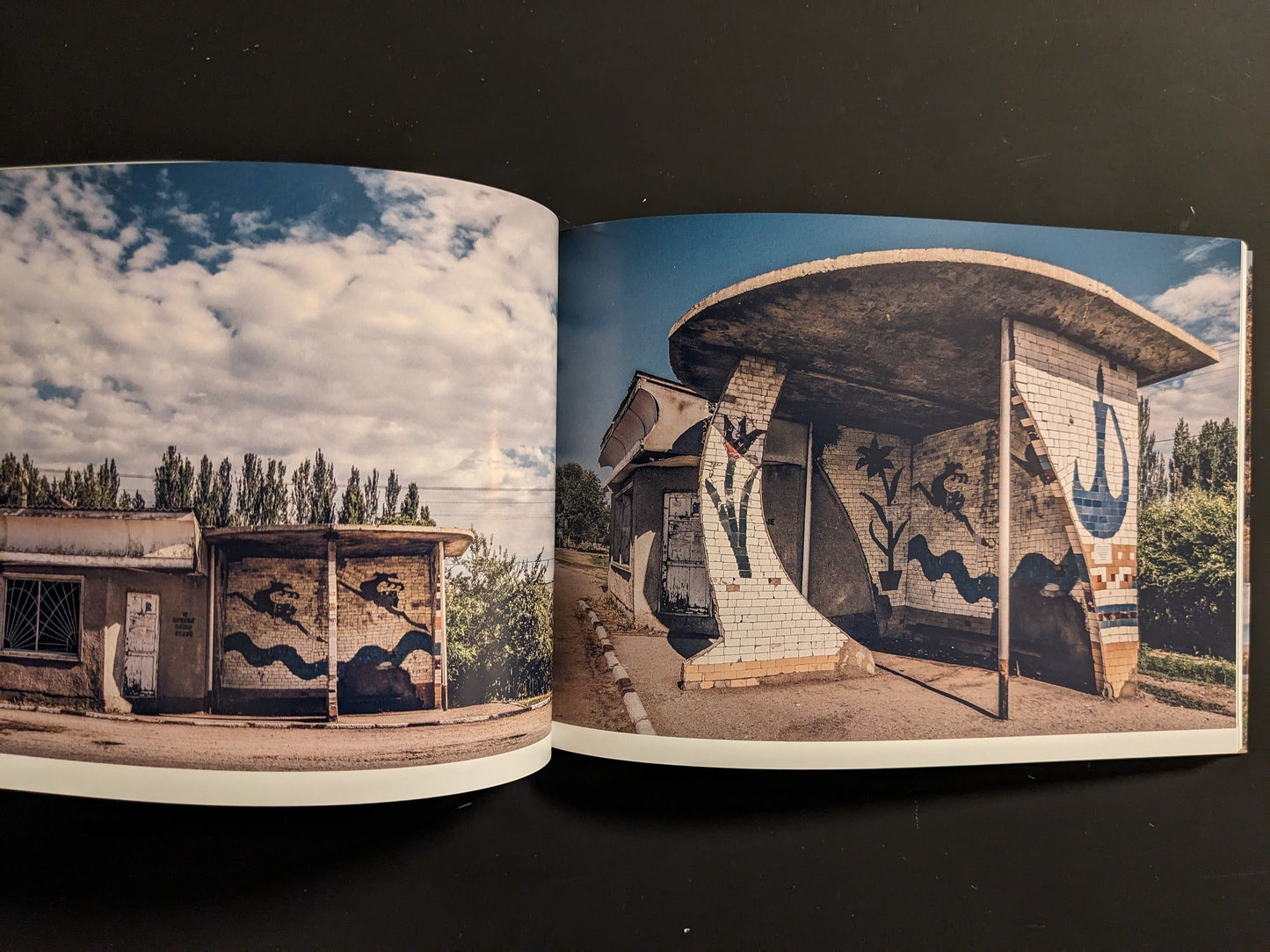 Interior spread with tiled bus shelters, curved walls, and painted murals beside a rural road.