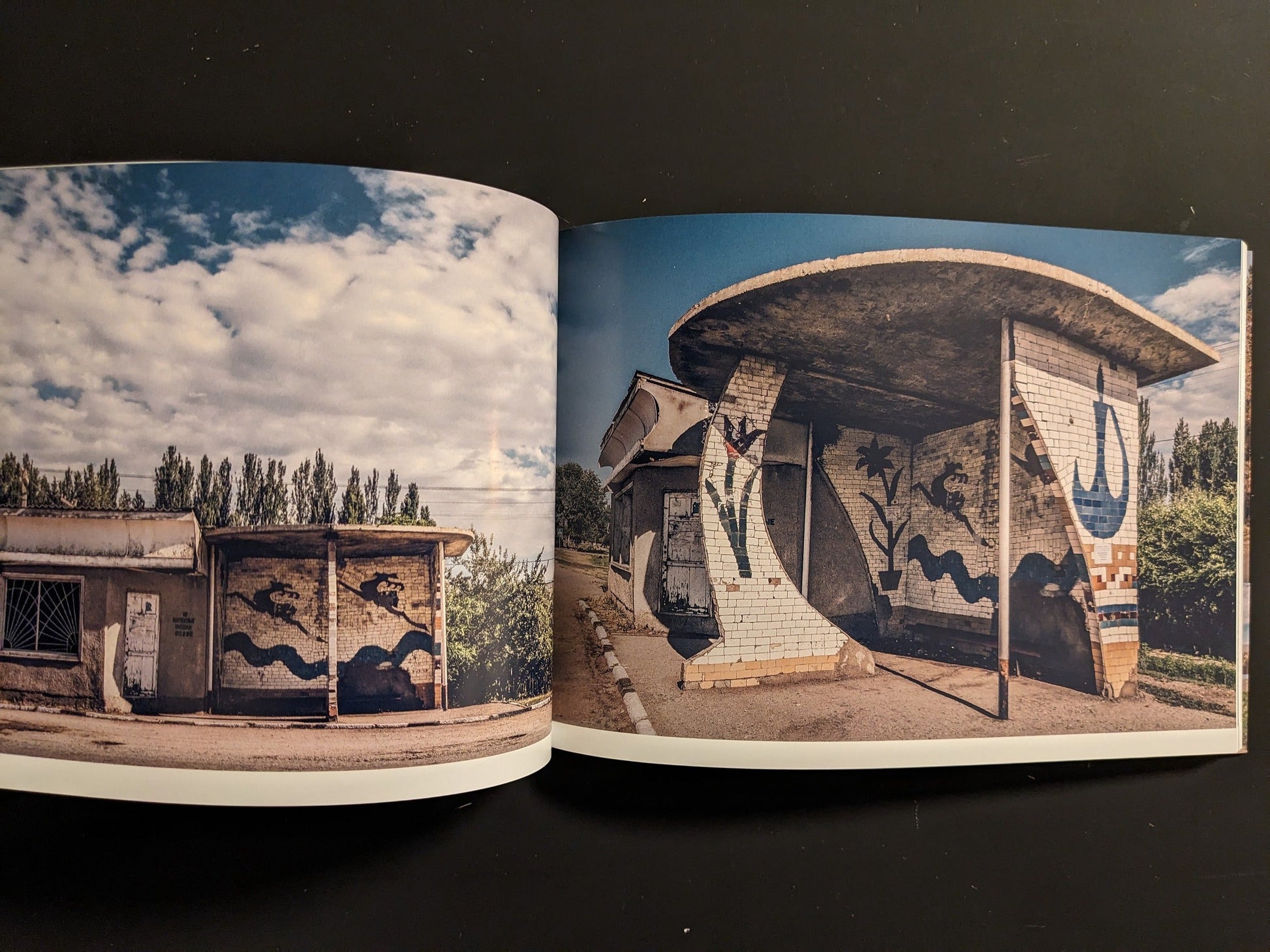 Interior spread with tiled bus shelters, curved walls, and painted murals beside a rural road.