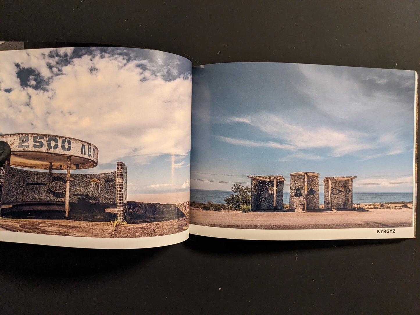 Interior spread: Kyrgyzstan chapter—three stone bus shelters in an open steppe landscape near water; wide sky.
