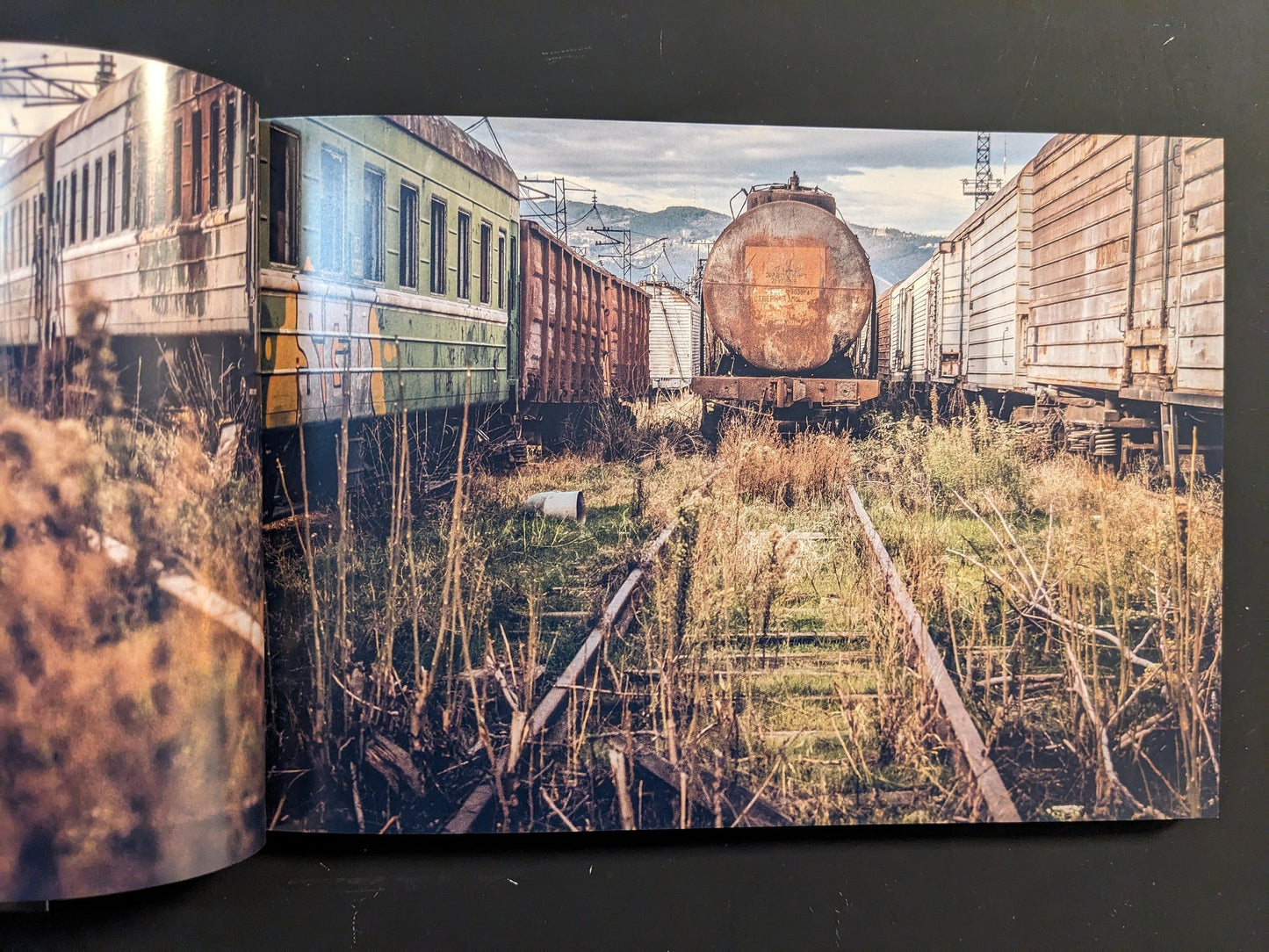 Interior spread: rusted freight cars and overgrown tracks in a derelict rail yard.