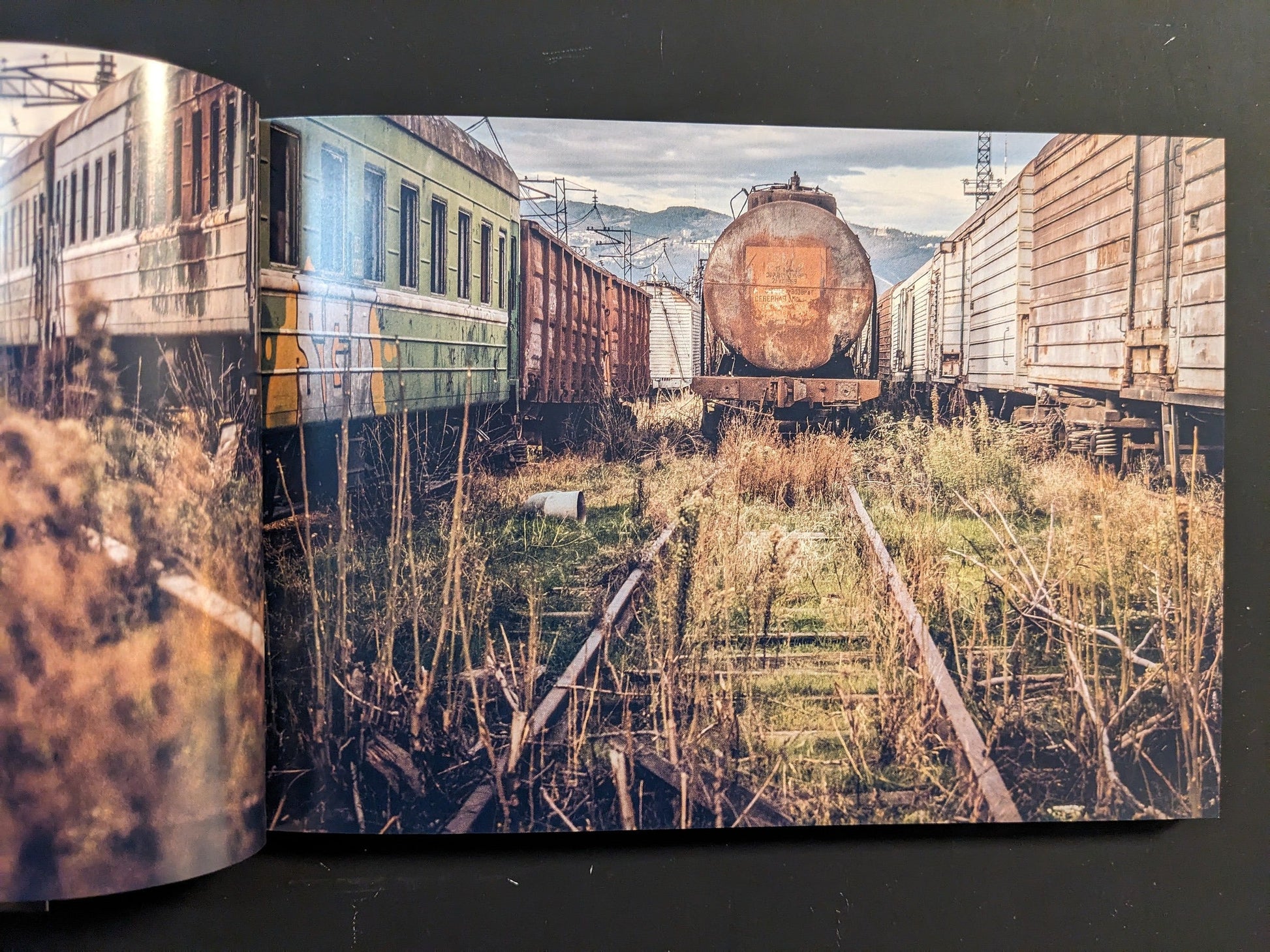 Interior spread: rusted freight cars and overgrown tracks in a derelict rail yard.