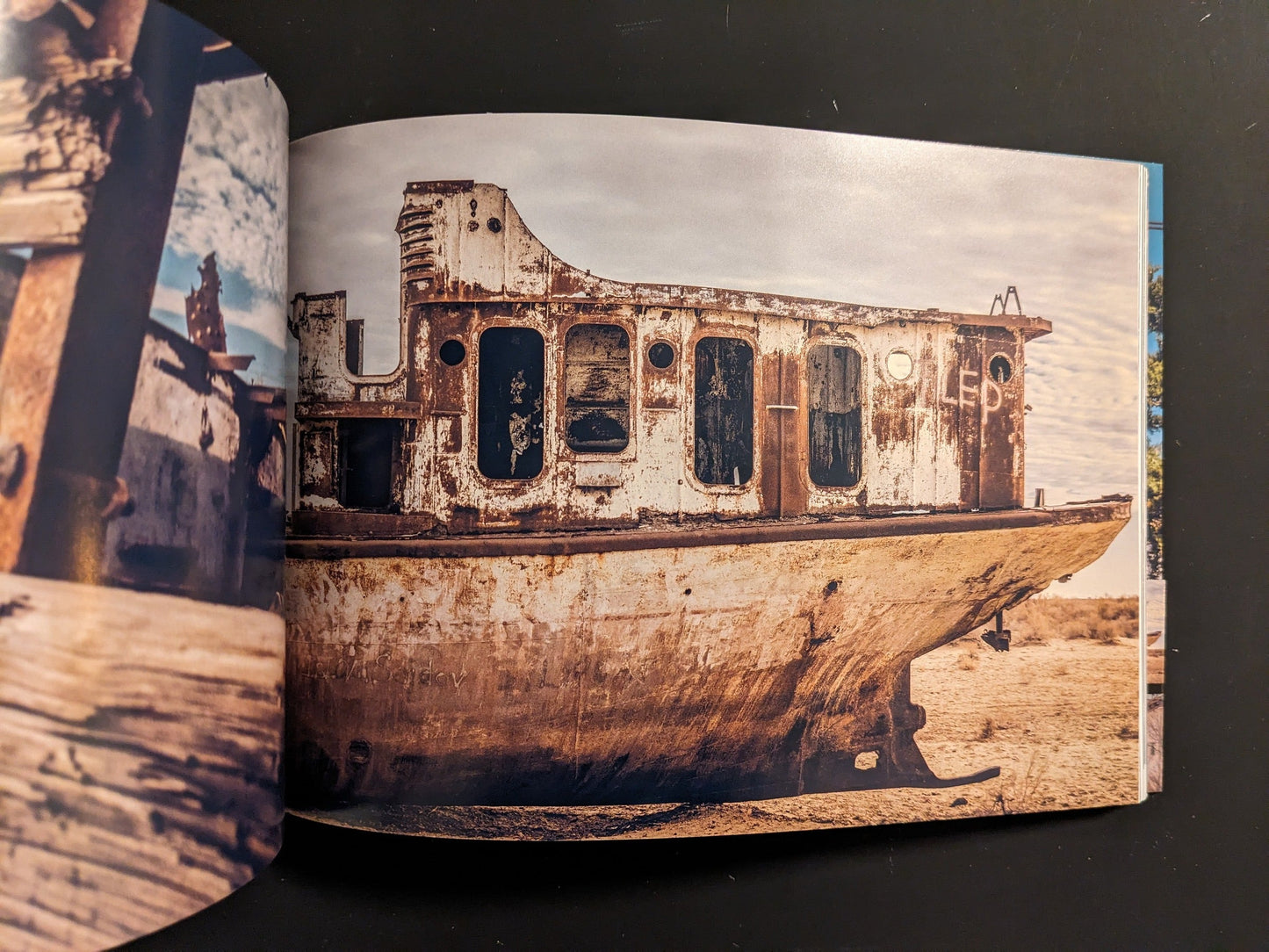 Beached, rusting ship hull in a barren desert landscape under a cloudy sky.