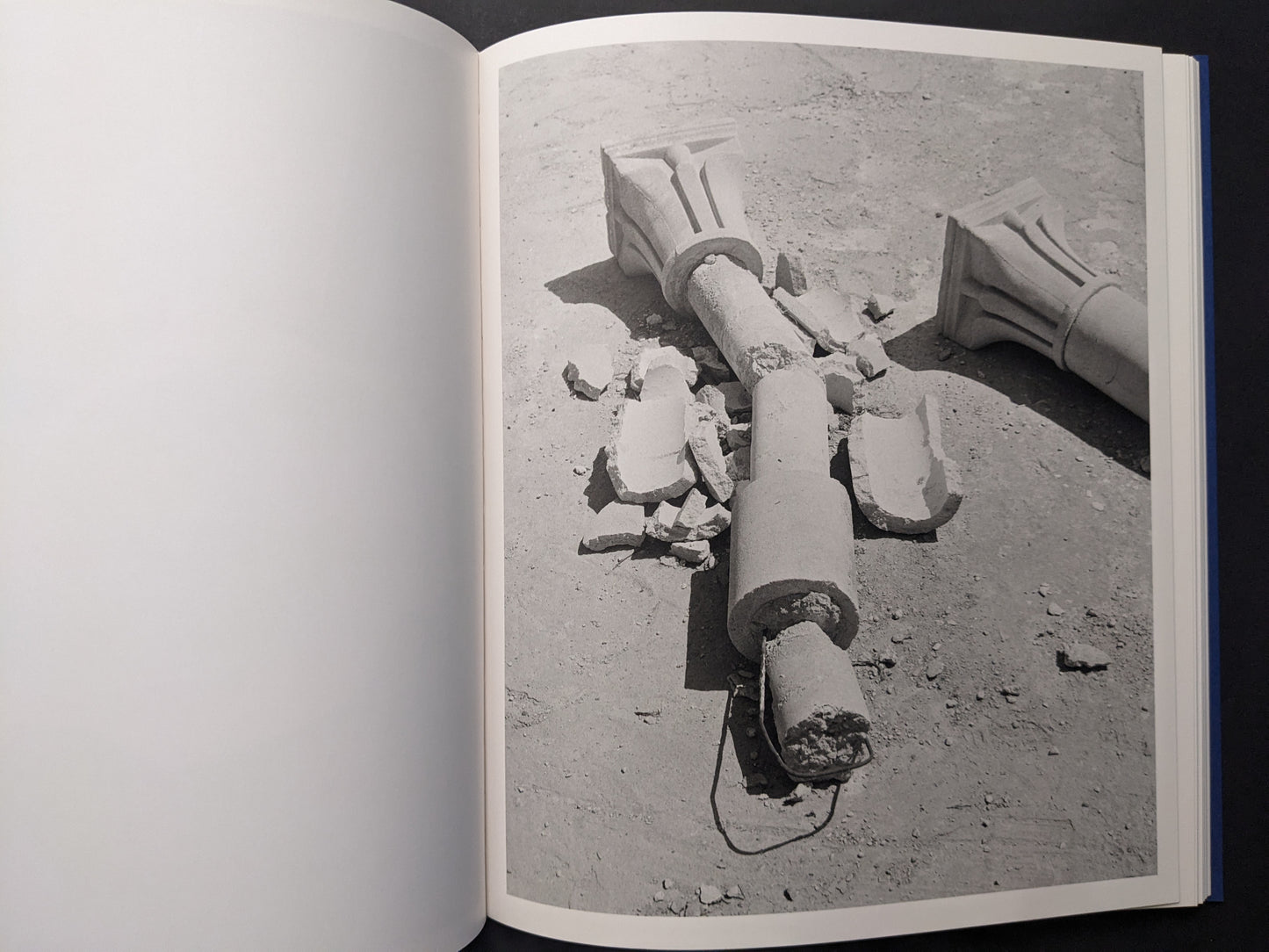 Black-and-white photograph of a broken column with fragments scattered on the ground.