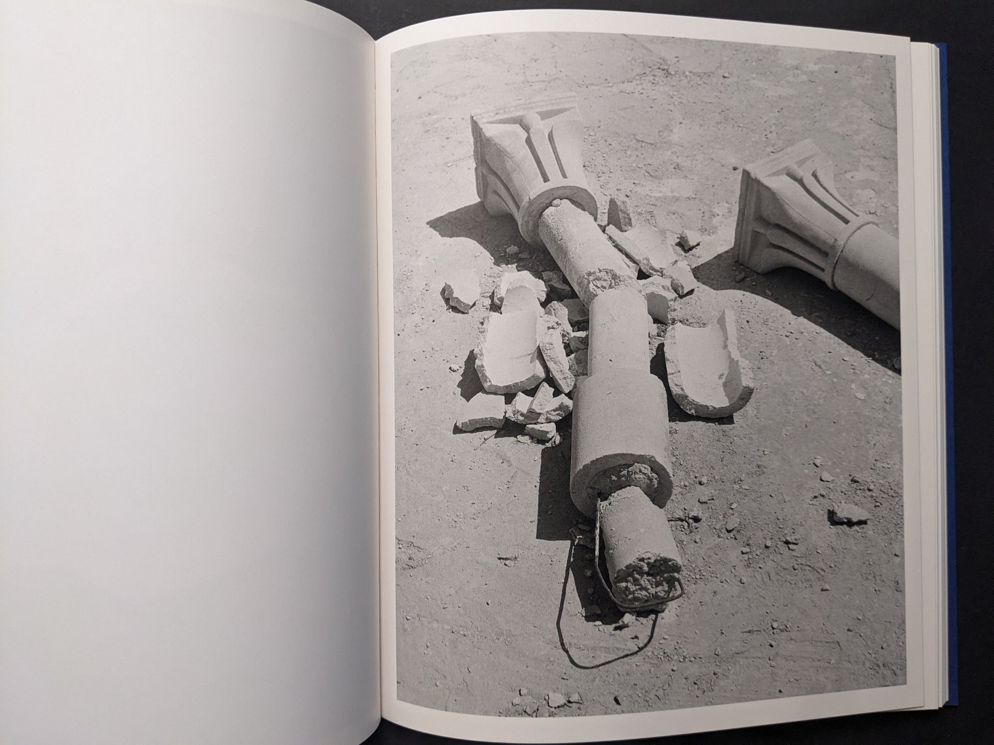 Black-and-white photograph of a broken column with fragments scattered on the ground.