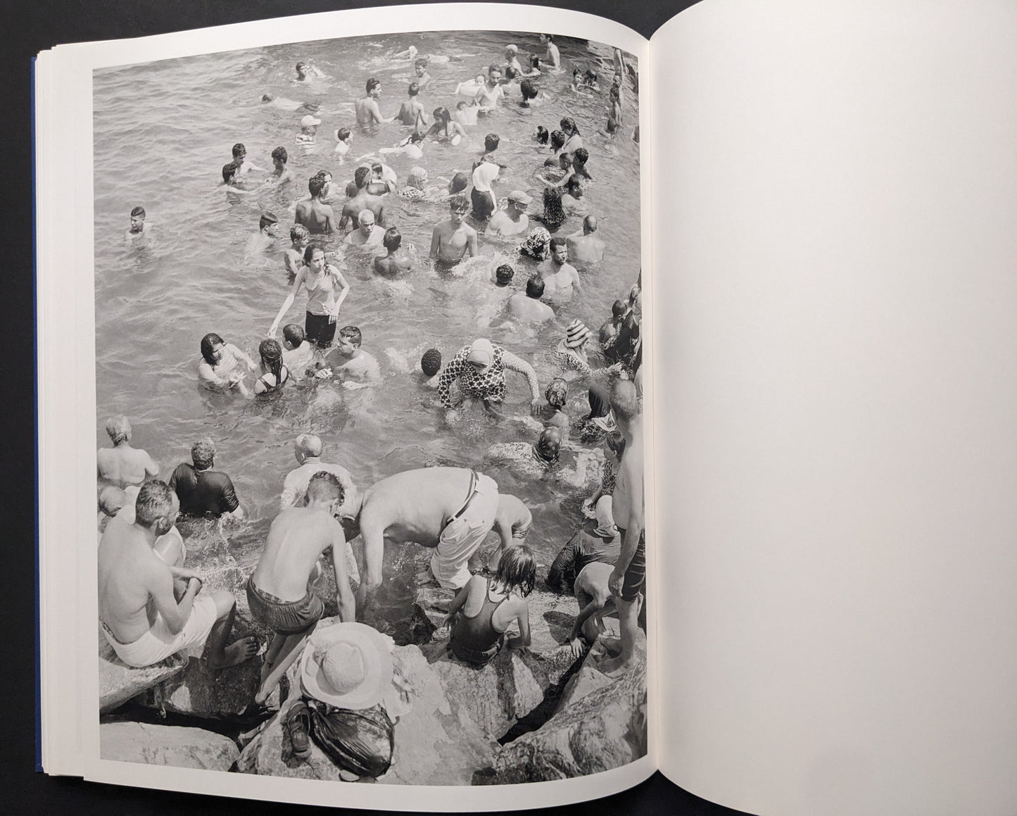 Black-and-white photograph of swimmers crowded in the sea near rocks.