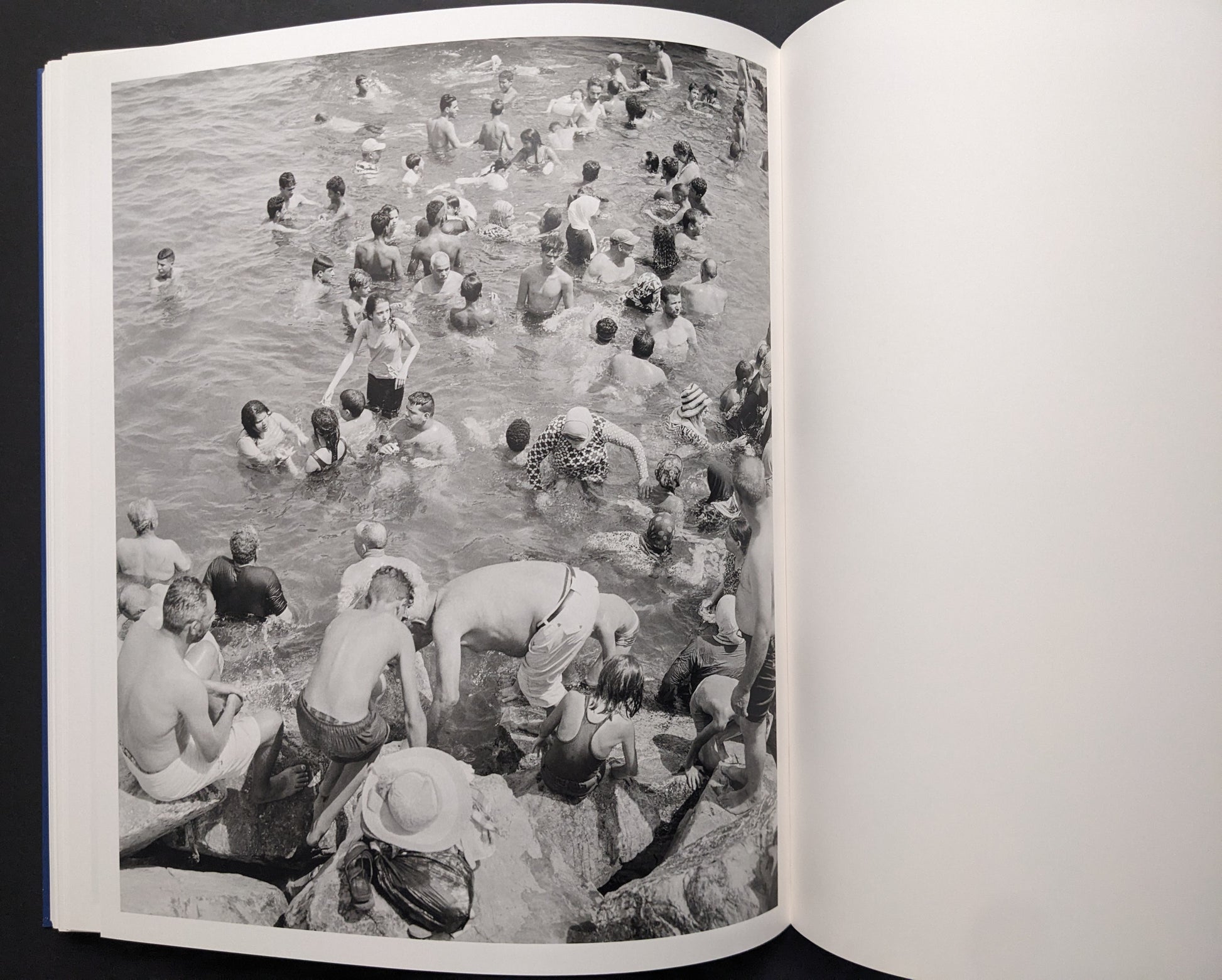 Black-and-white photograph of swimmers crowded in the sea near rocks.