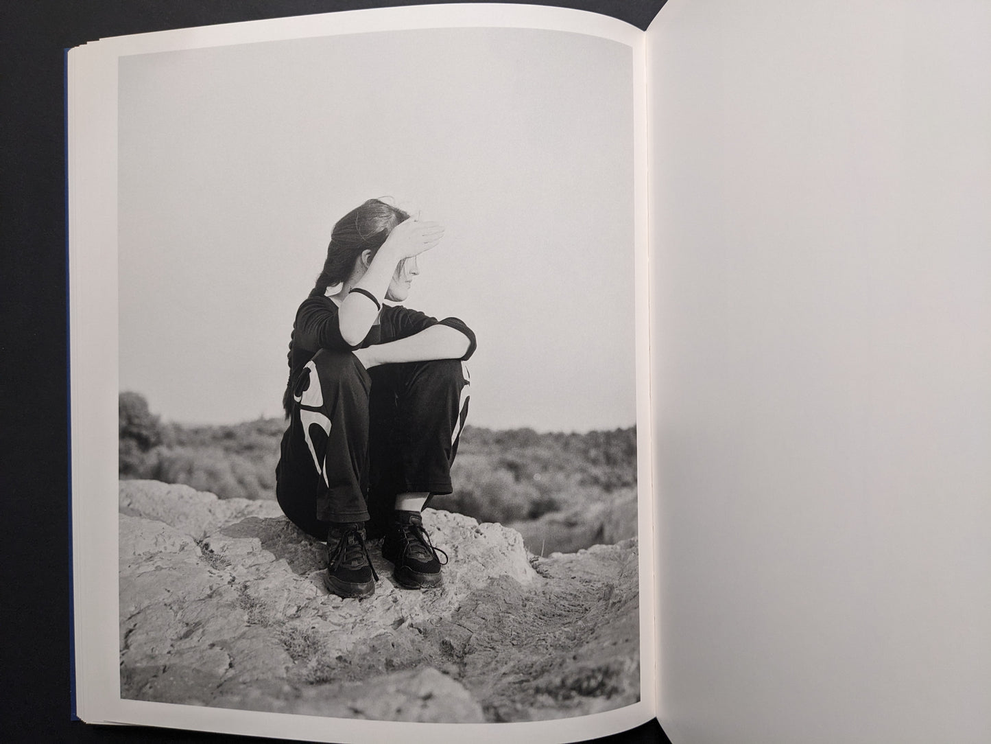 Black-and-white portrait of a seated figure shading their eyes from the sun.