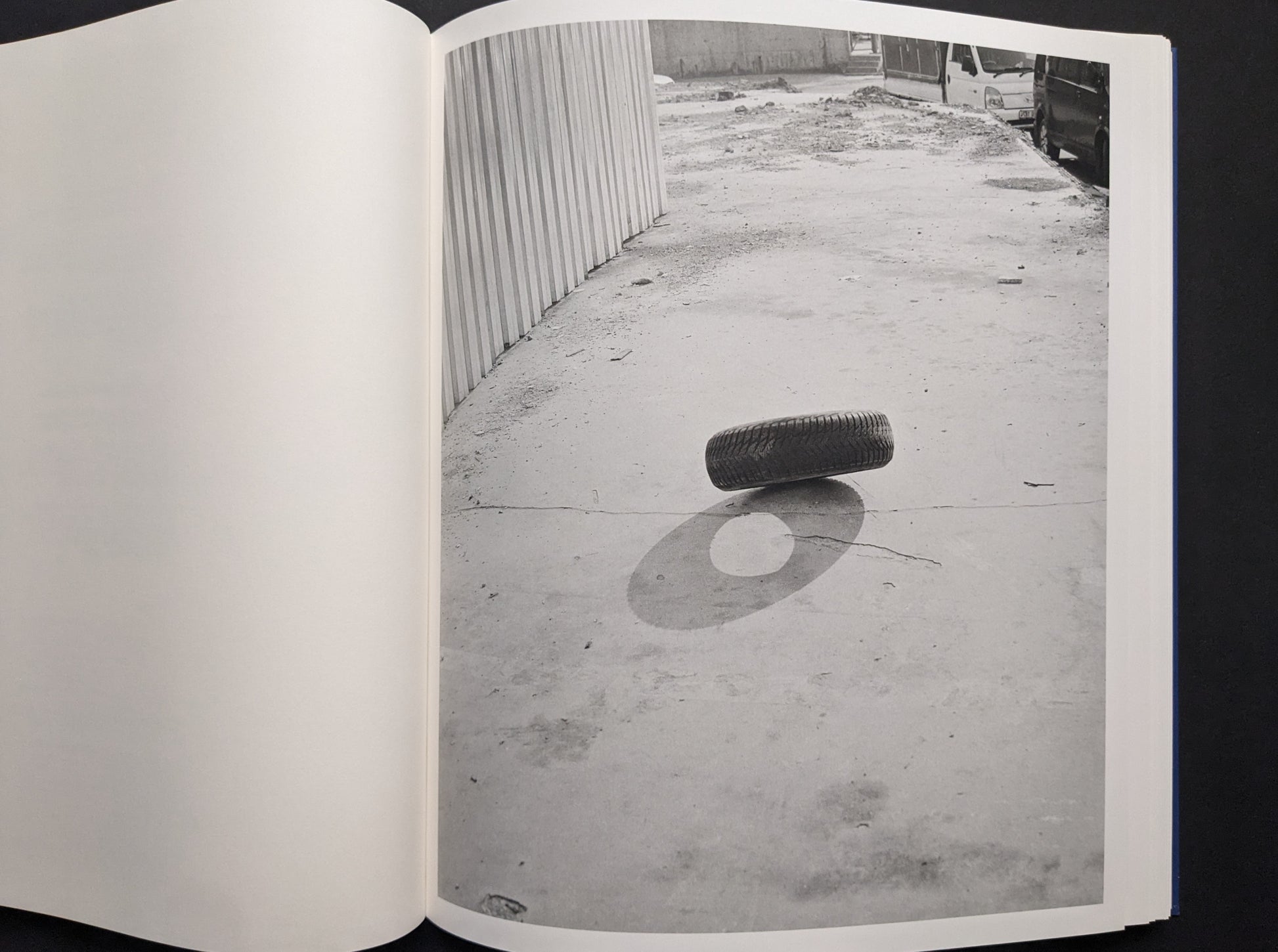 Black-and-white photo of a tire balanced on its edge, casting a sharp shadow.