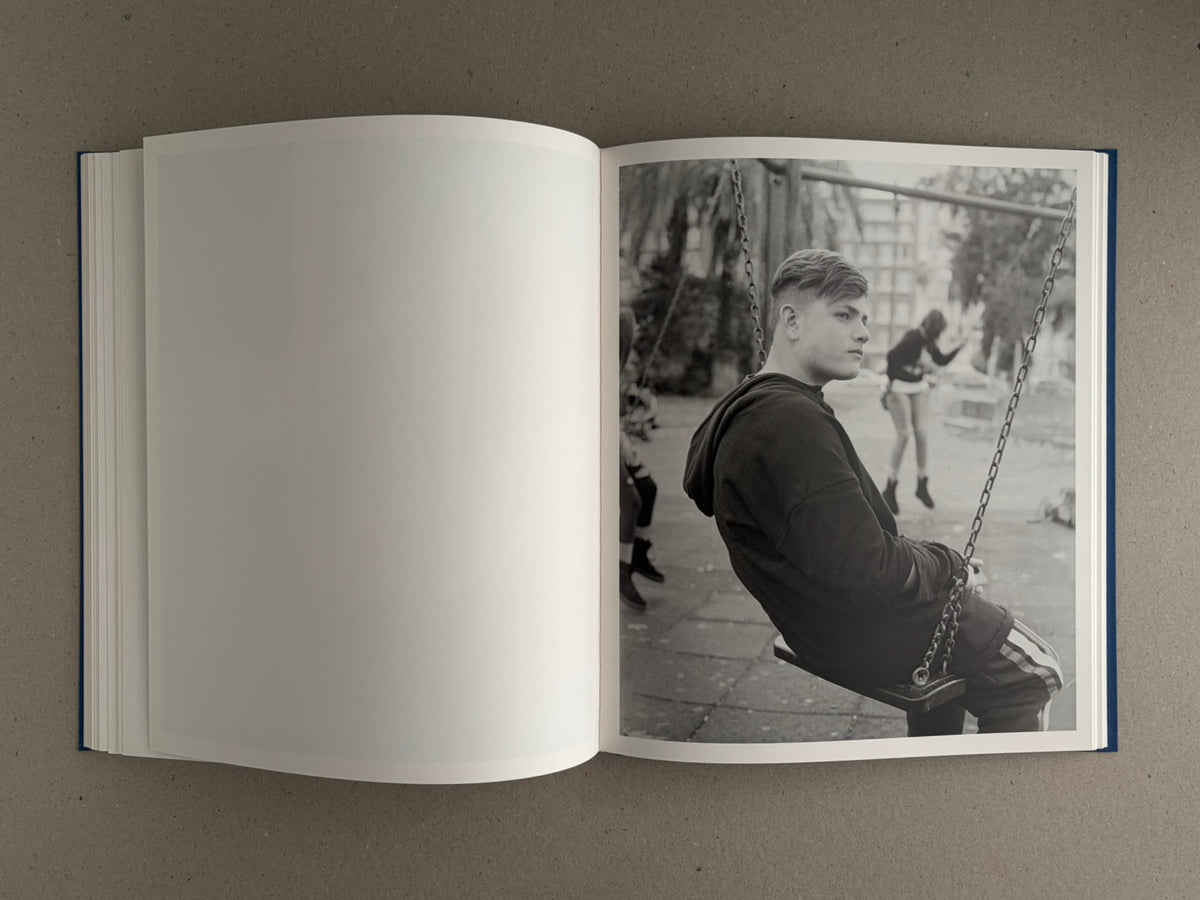 Sub Sole – Massao Mascaro open book spread with a black-and-white photograph of a young person seated on a swing on the right page and a blank left page.
