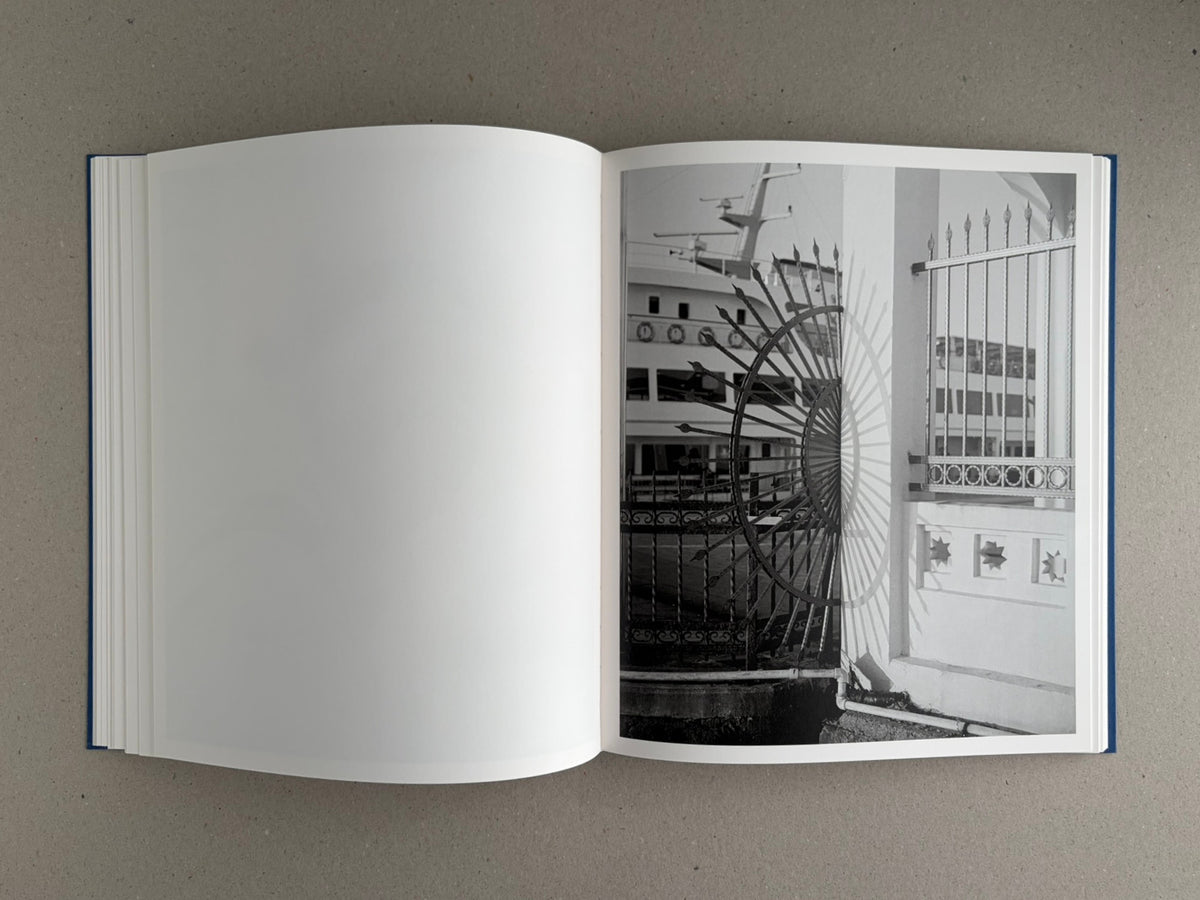 Open spread of Sub Sole by Massao Mascaro, with a blank left page and a black-and-white photograph on the right page showing a metal gate and building facade.