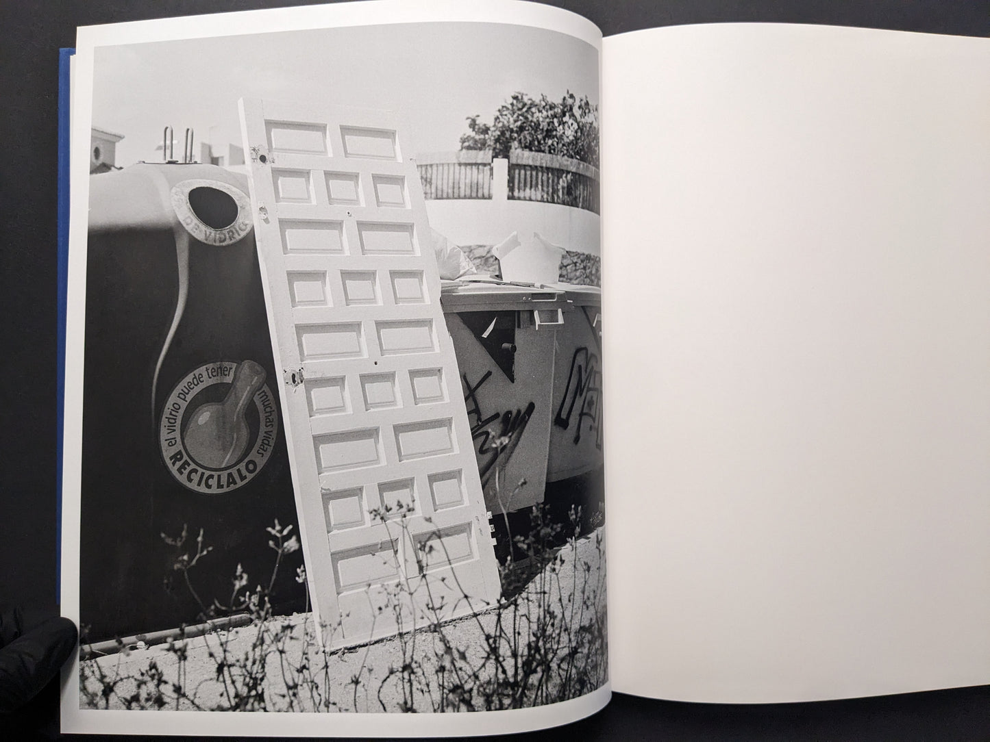Black-and-white photograph from Sub Sole by Massao Mascaro showing a discarded door leaning among large containers and debris.