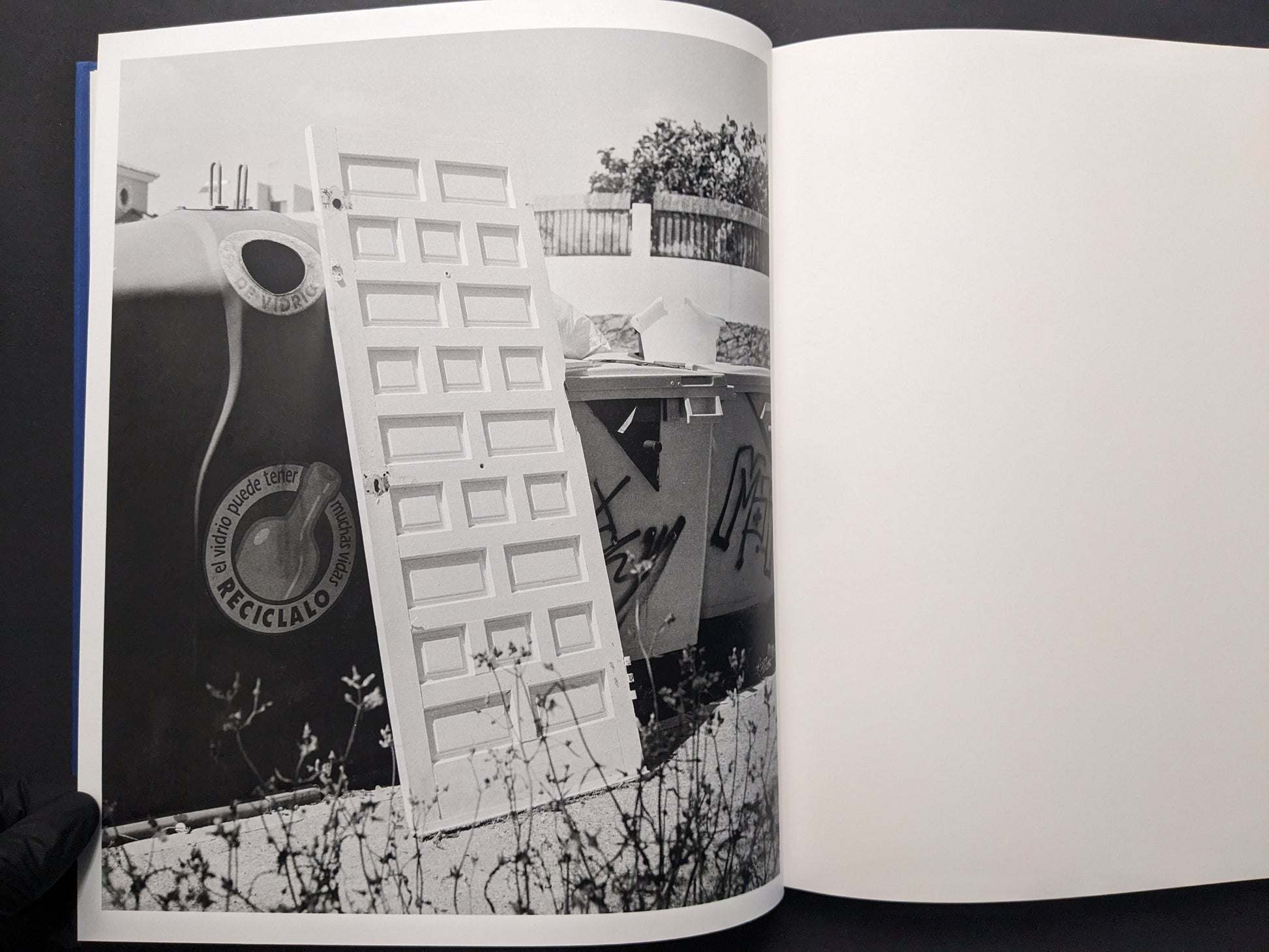 Black-and-white photograph from Sub Sole by Massao Mascaro showing a discarded door leaning among large containers and debris.
