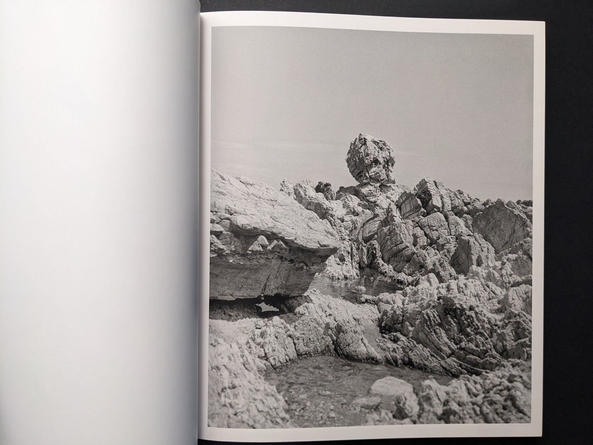 Black-and-white photograph of jagged rocks and a coastal landscape under open sky.